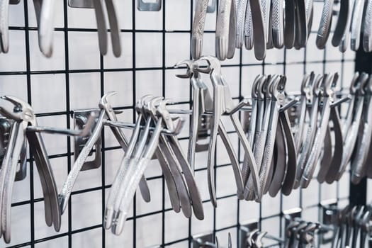 perspective view closeup of row of various stainless steel dental extraction forceps tools hanging on display