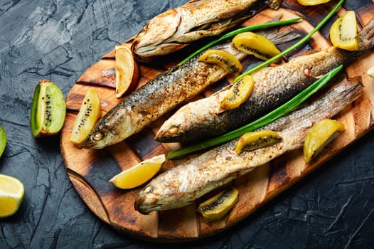 Prepared grilled fish with kiwi and lime on kitchen board. Healthy food