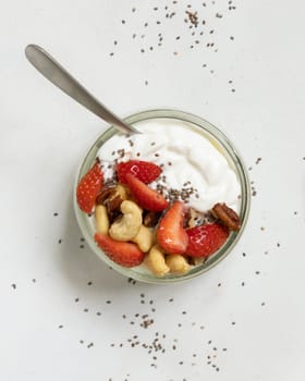 Greek yogurt, nuts and strawberries in a glass jar with a spoon on a white table top view. Healthy breakfast with fruits and nuts. Great way to eat protein