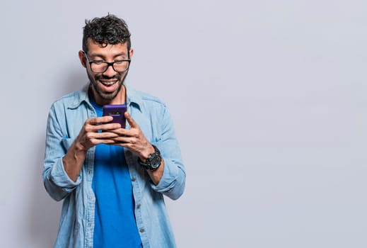 Smiling handsome boy texting with his cell phone isolated, young latin man happy with his cell phone isolated, happy teenager texting with his cell phone