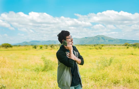 A man in a beautiful field talking on the phone, person with cell phone calling on the phone in the field, people talking on the cell phone in the field. Man calling on the phone in the field