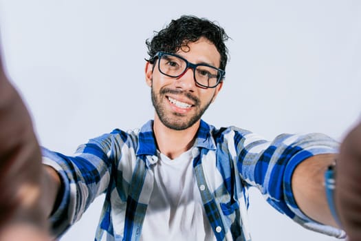 Handsome man taking a selfie looking at the camera on isolated background. Teenage guy taking a self portrait isolated. Guy with beard and glasses taking a self portrait isolated
