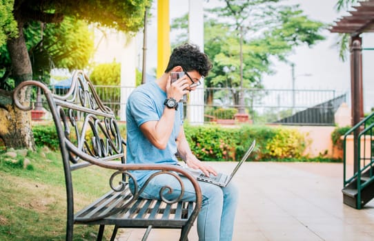 Man in a park working online with laptop and calling on cellphone. Freelancer man working with laptop while calling on the phone, Young man sitting in a park working with his laptop and cell phone