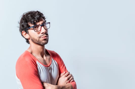 Portrait of young man with crossed arms isolated. Young latin man in glasses with crossed arms looking in profile at the camera. Nicaraguan man with crossed arms looking at the camera isolated