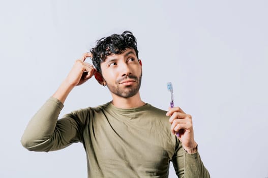 Thoughtful man holding toothbrush isolated, Portrait of young man thinking holding toothbrush. Man holding toothbrush with pensive expression isolated. Person holding toothbrush looking up