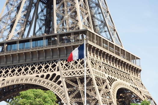The Eiffel Tower in Paris, France with the french flag in front of it.