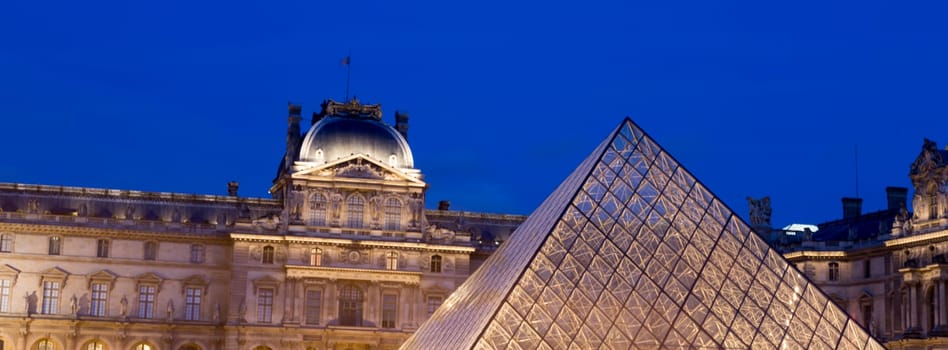 The Louvre at Night in Paris, France with blue sky.