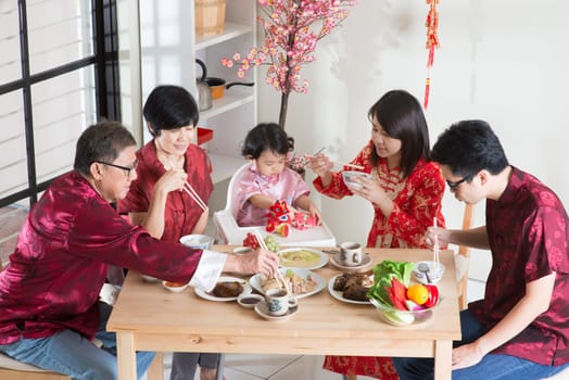 Celebrating Chinese New Year, reunion dinner. Asian multi generation family with red cheongsam dining at home.