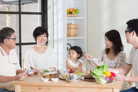 Happy Asian Chinese multi generations family dining at home. Eating with chopsticks.
