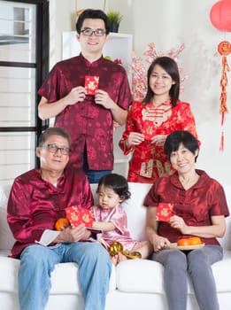 Celebrating Chinese new year. Happy Asian multi generations family in red cheongsam showing red packets while reunion at home.