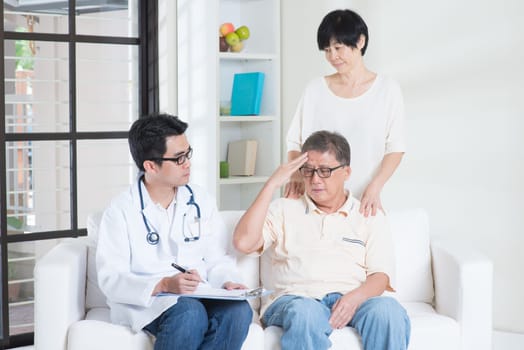 Doctor and patient. Asian old man headache, consult family doctor, sitting on sofa. Senior retiree indoors living lifestyle.