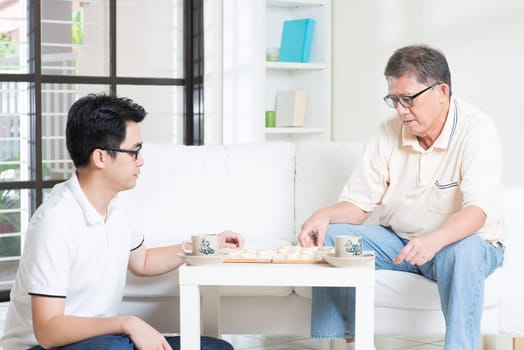 Chinese family playing Chinese chess (Xiang Qi) at home, senior father and adult son.