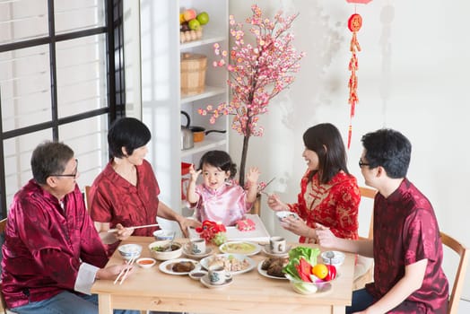 Celebrating Chinese New Year, reunion dinner. Happy Asian Chinese multi generation family with red cheongsam dining at home.