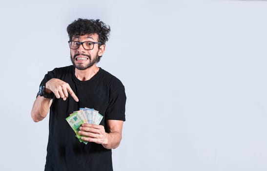Handsome man pointing at the money in his hand isolated, a person pointing at money bills in his hand, concept of earnings and savings