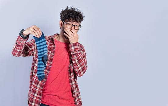 Handsome man with a smelly sock in his hand holding his nose isolated. Person with a stinky sock in his hand, concept of smelly socks and uncleanliness