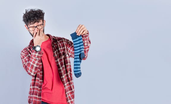 Man with a smelly sock in his hand holding his nose. Person with a stinky sock in his hand, concept of smelly socks and uncleanliness
