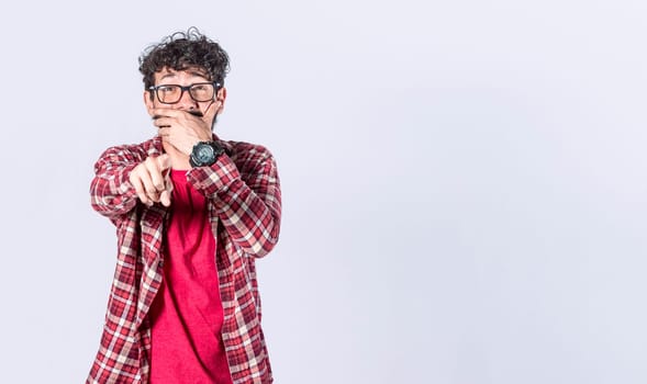 Isolated attractive guy laughing at you, young man pointing at camera with hand over mouth, male making fun of you
