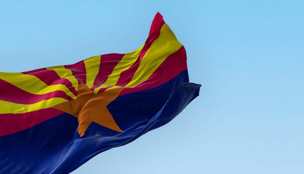 The flag of Arizona waving in the wind on a clear day. Copper star, 13 rays of red and yellow, and a blue bottom half. 3d illustration render. Fluttering textile