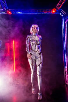 Blonde as a cyber robot. Girl in shining silver armor in neon. She walks in a glowing cube, smoke around. Blonde with fantastic makeup and image in a dark key and colored light, posing in cyberspace.