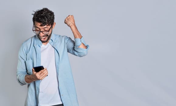 Happy person holding a smartphone and celebrating isolated, Excited man winning a prize from his cellphone. Excited handsome man looking at smartphone celebrating something