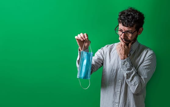 Thoughtful man deciding which surgical mask to wear, Thoughtful person holding a surgical mask isolated, People thinking while holding a surgical mask