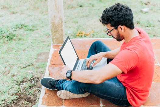 Side view of student man sitting cross-legged on the floor with his laptop, concept of person sitting on the floor typing on his laptop, Teenage student sitting on the floor working on his laptop