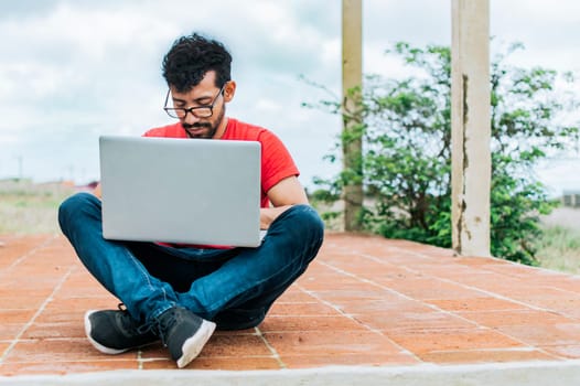 Teenage student sitting on the floor working on his laptop, young man sitting cross-legged on the floor with his laptop, concept of person sitting on the floor typing on his laptop