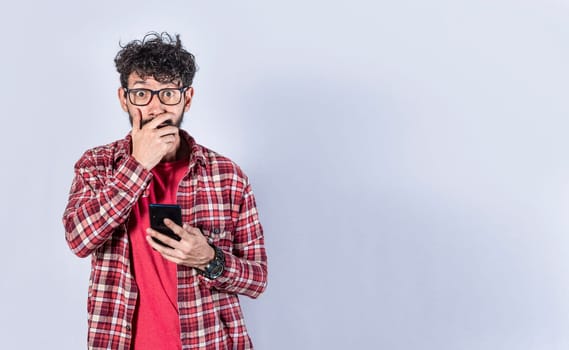 Man holding his cell phone and covering his mouth. surprised man receiving news on his cell phone isolated. Astonished man holding his cellphone and covering his mouth isolated