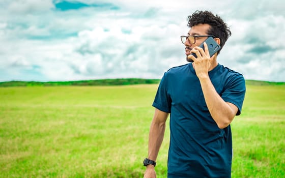 Handsome man calling on the phone in the field. man on the road talking on the phone, person in the field calling on the phone, young man talking on the phone in the field looking to the side