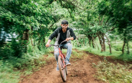 Portrait of a guy in cap riding a bike on a country road, Person riding a bike in the countryside, Bicyclist person on his bike on a country road forest. Teenage guy riding a bike in the countryside