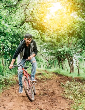 Person riding a bike in the countryside, Portrait of a guy in cap riding a bike on a country road, Bicyclist person on his bike on a country road forest. A guy riding a bike in the countryside