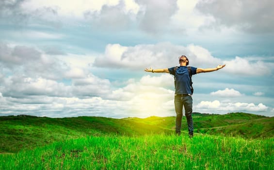 Adventurous man spreading his arms in the countryside. Man with backpack on a hill spreading his arms. Explorer man spreading his arms on a hill. Lifestyle of adventurous man in the field