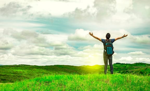 Man with backpack on a hill spreading his arms. Adventurous man spreading his arms in the countryside. Explorer man spreading his arms on a hill. Lifestyle of adventurous man in the field