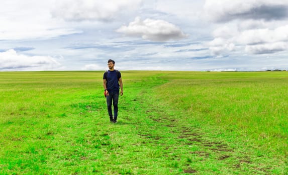 Traveler man walking in the beautiful countryside. Backpacker man walking in a countryside. Landscape of traveler man walking in the green field. Lifestyle of adventurous man in the field