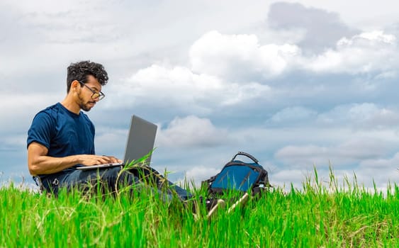 Freelancer man sitting with laptop and backpack in the field. Man sitting in the green field working from his laptop. Freelancer man concept working from the field