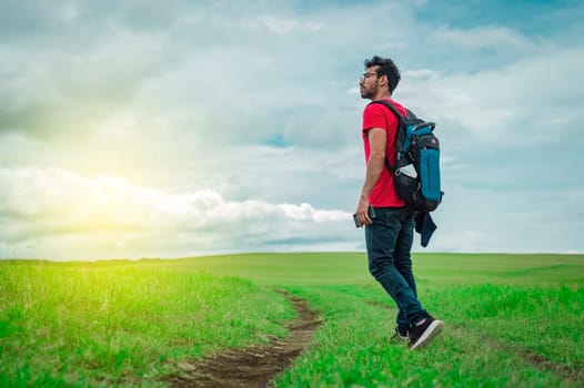 Side view of backpacking man on a beautiful road in the countryside. Young explorer man walking in a green field, Backpacker man walking in a beautiful field.