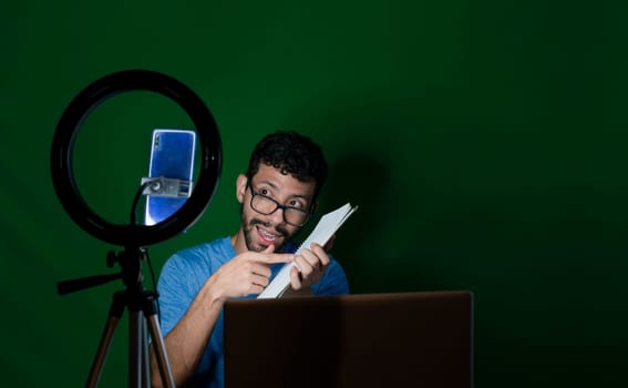 Person giving classes in a video call. Man giving online classes with phone. Guy with laptop making video blog on phone. Guy on a video call working from home. Online classes concept