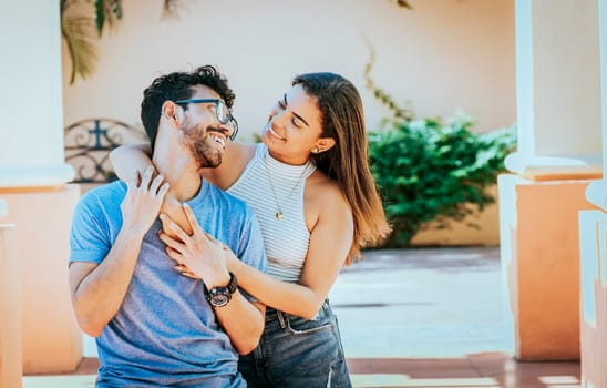 Girl hugging her boyfriend from behind. Smiling woman hugging her boyfriend from behind while he smiles at her, Happy couple, woman hugging man from behind outdoors