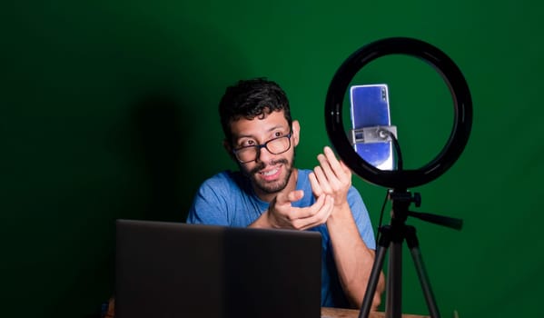 People giving online classes with phone. Guy with laptop making video blog on phone. Person giving classes in a video call. Guy on a video call working from home. Online classes concept