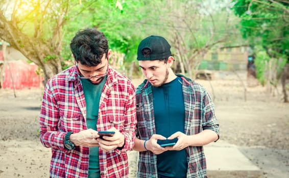 Jealous friend spying on his friend's cellphone outdoors, Friend spying on his friend phone. A guy snooping on his friend's phone on the street, Concept of jealous friends with cellphone