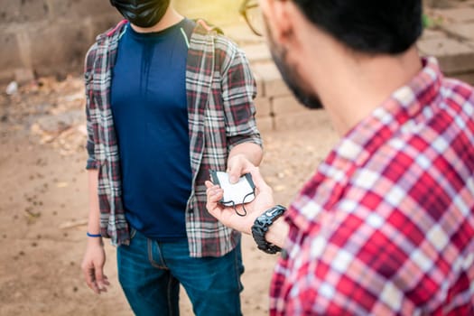 A young man giving a surgical mask to another person, concept of a person giving a surgical mask, Two young people giving each other a surgical mask