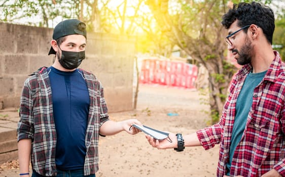 Side view of young man giving a surgical mask to another person, concept of a person giving a surgical mask, Two young people giving each other a surgical mask