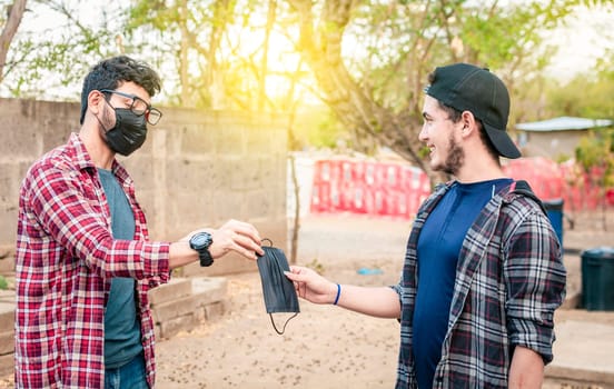 Concept of a person giving a surgical mask, Two young people giving each other a surgical mask, Side view of young man giving a surgical mask to another person outdoor