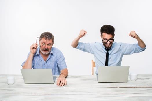 The two colleagues working together at office on white  background. both men are looking at the computer screens. a young man getting good news. the old man is upset. concept of competition in business and jealousy