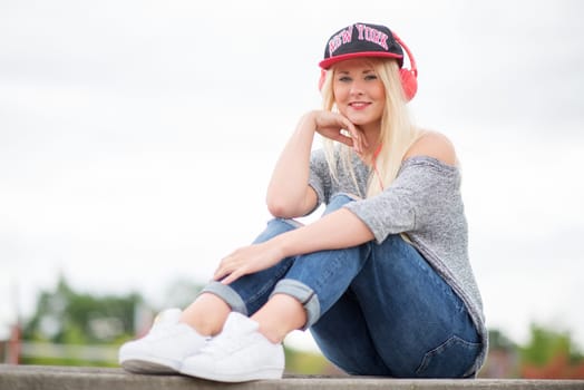 Girl with headphones and basecap listens to music outside