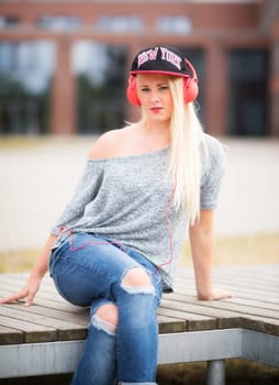 Young woman in jeans sits outside listening to music