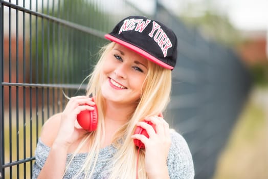 Girl with headphones stands outside on a fence