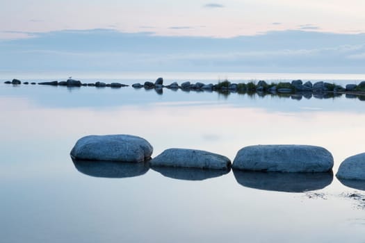 Breakwater Rocks in Calm Sea with clouds and reflextions in the water.
