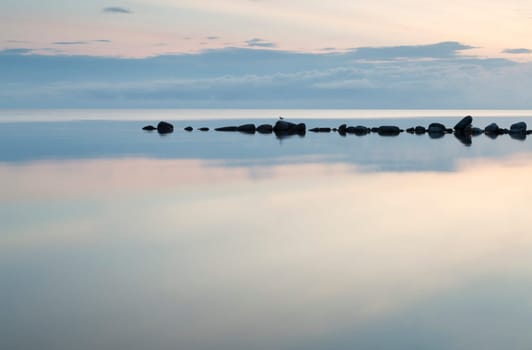 Breakwater Rocks in Calm Sea with clouds and reflextions in the water.
