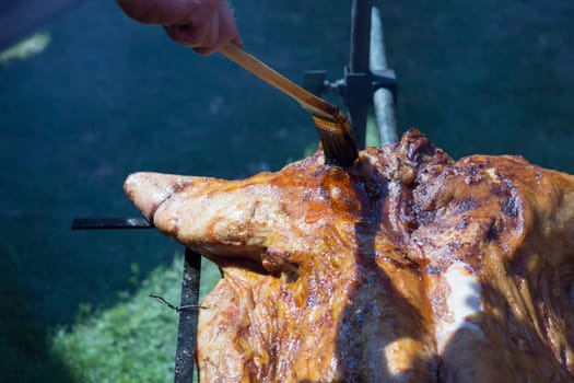 Barbecuing Pork a Complete Pig with marinade being penseled on.